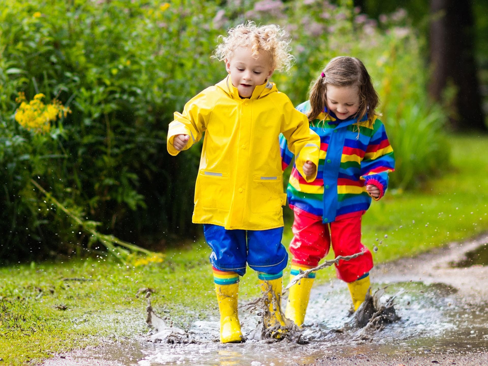 Tolle Pfützenspiele für Regentage gibt es hier. Kinder spielen in Pfützen.