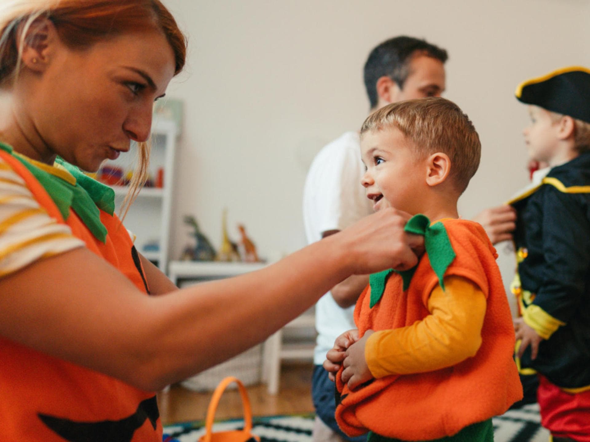Halloween-Kostüme müssen nicht kompliziert sein, es geht auch schnell und einfach! Frau passt Kind ein Kürbiskostüm an.