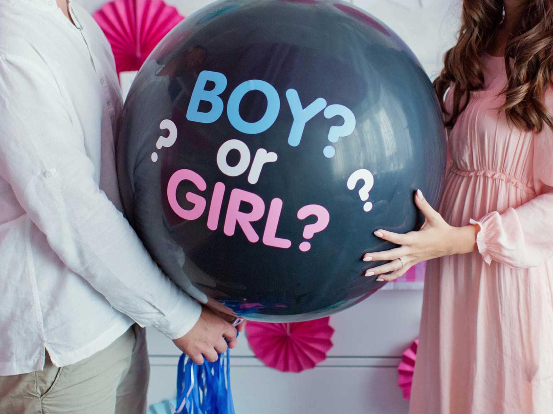 Mädchen oder Junge? Das ist bei einer Gender Reveal Party die alles entscheidende Frage. Werdende Eltern halten großen Ballon mit Aufschrift "boy or girl?".