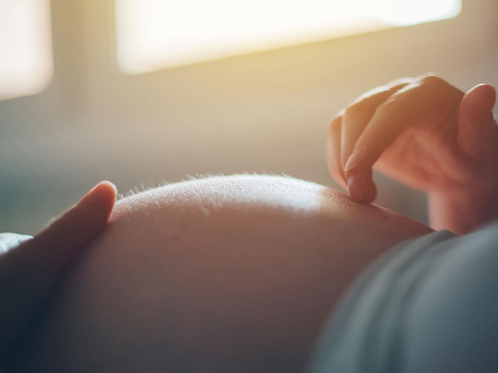 Eine Dammmassage hilft bei der Geburtsvorbereitung. Schwangere berührt ihren Bauch mit Händen.
