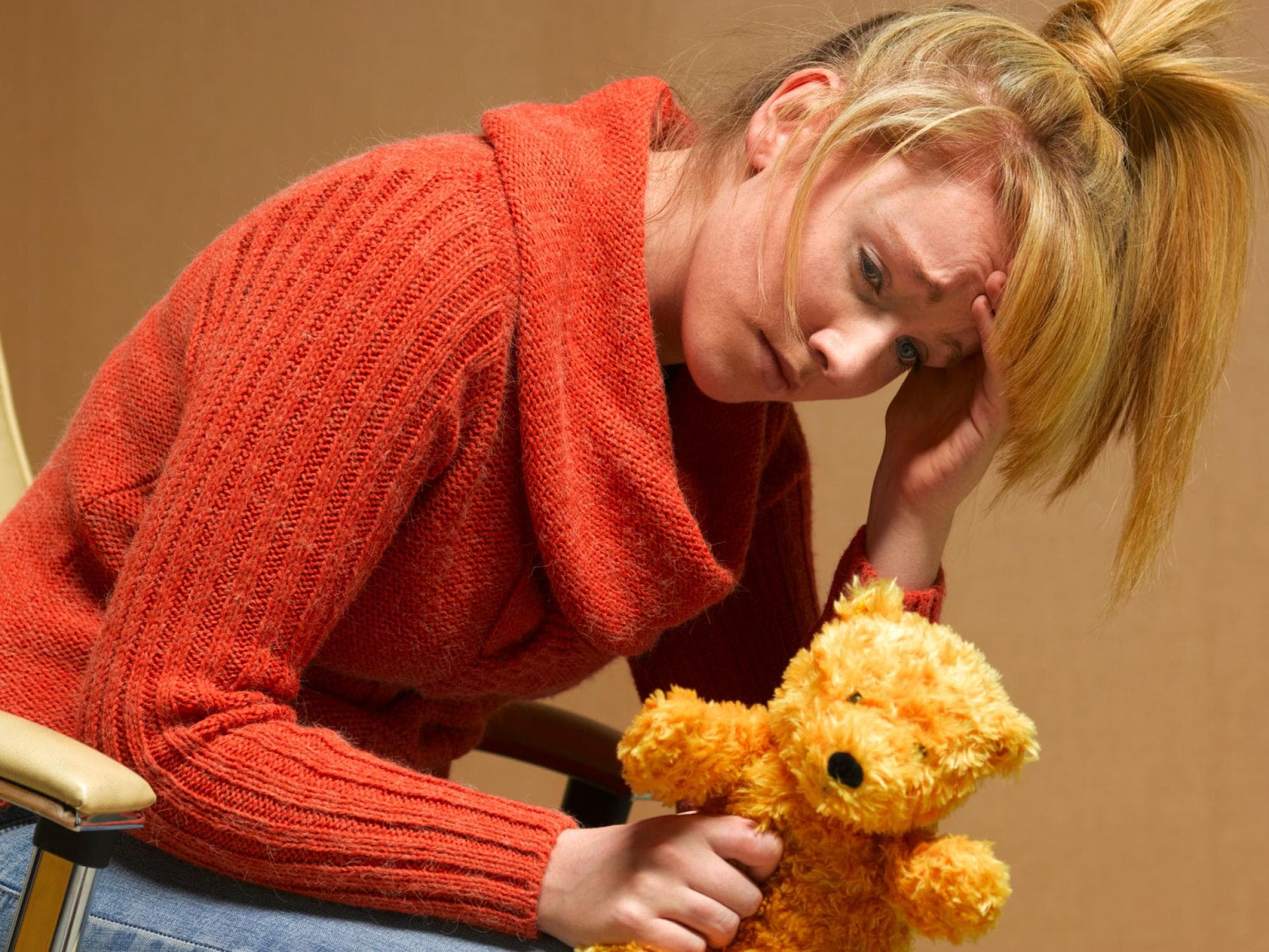 Bei einer postpartalen Depression erscheint alles schwer. Erschöpfte, mutlose Frau mit Teddy in der Hand.