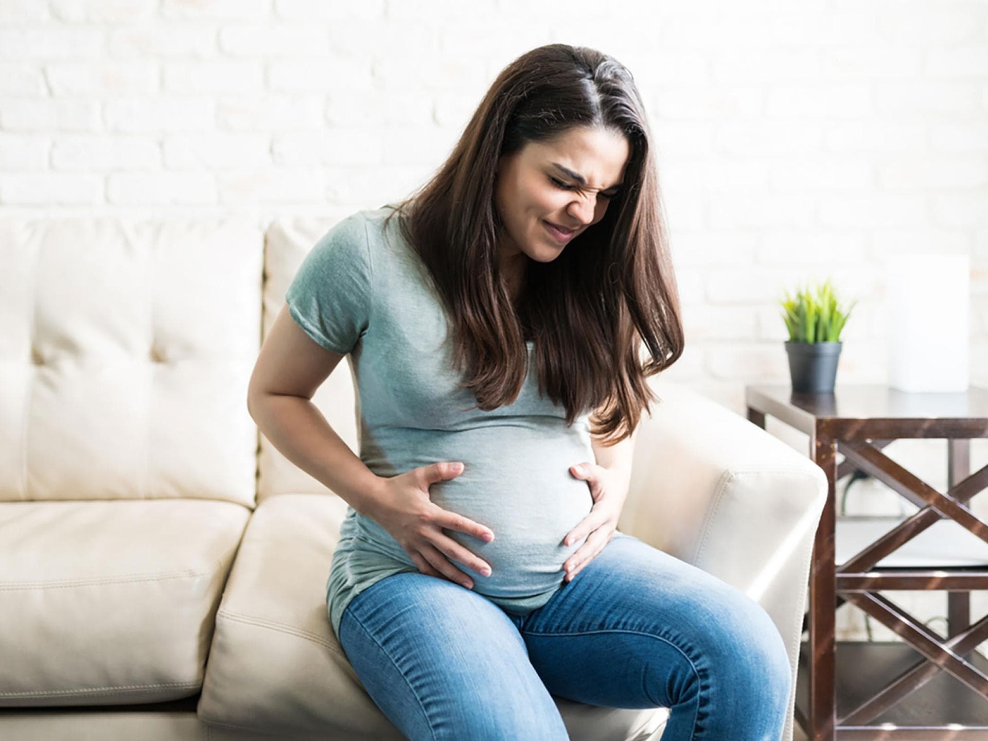 Gerade kurz vor der Geburt fragen sich viele Schwangere, wie sich Wehen anfühlen? Eine schwangere Frau mit schmerzverzerrtem Gesicht hält ihren Babybauch.