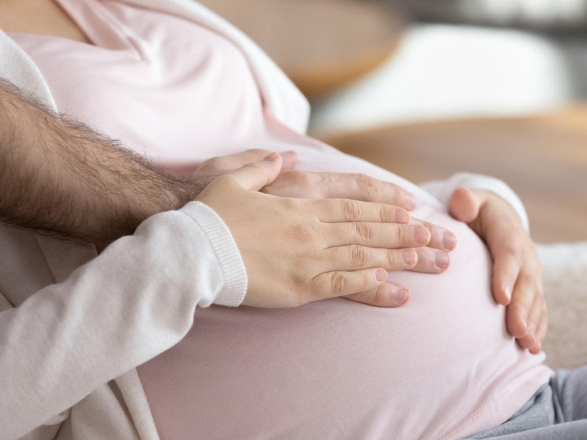 Frau und Mann legen Hände auf Babybauch.