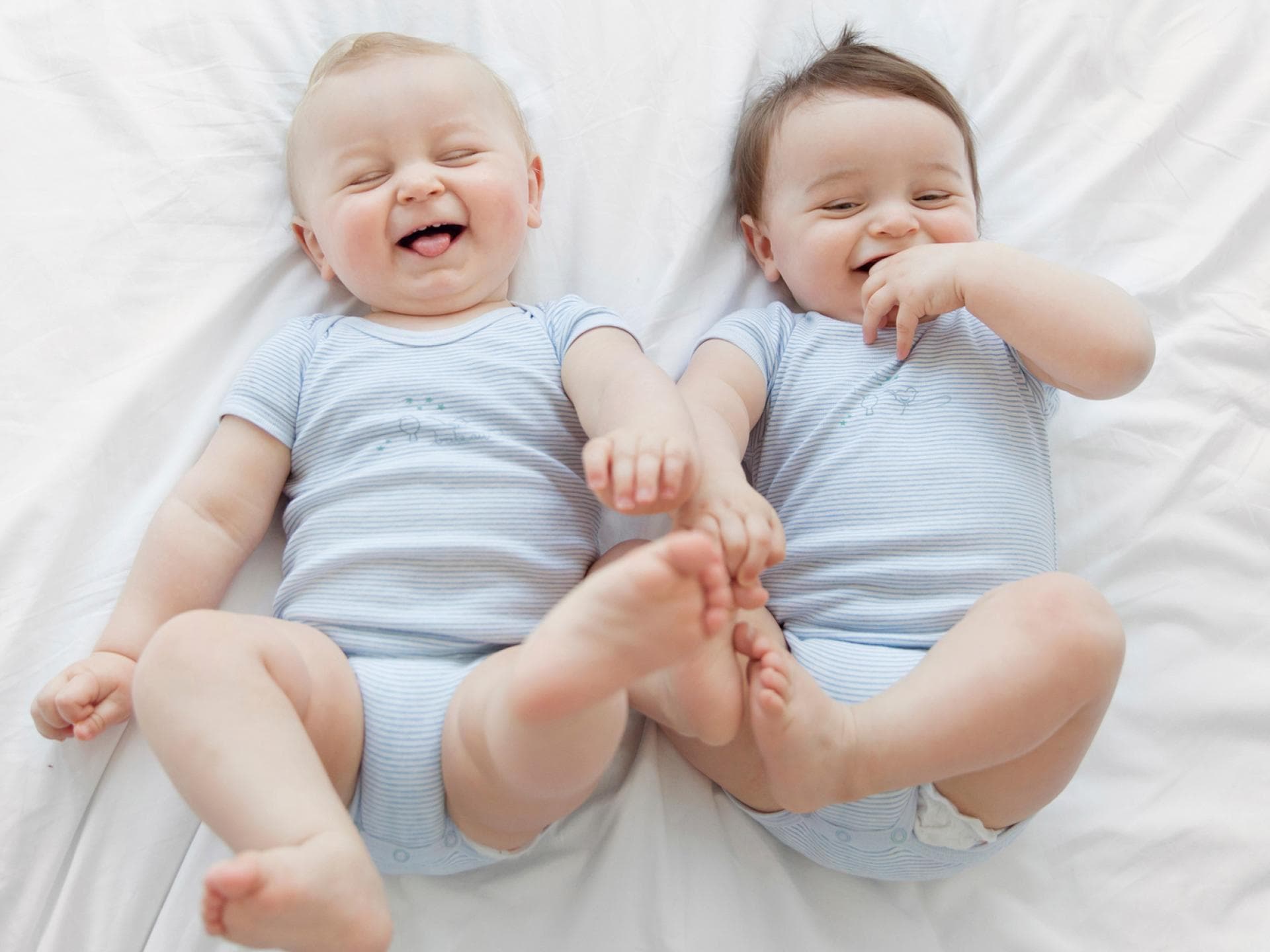 Zwillinge sind etwas ganz Besonderes. Baby-Zwillinge liegen nebeneinander und lachen.