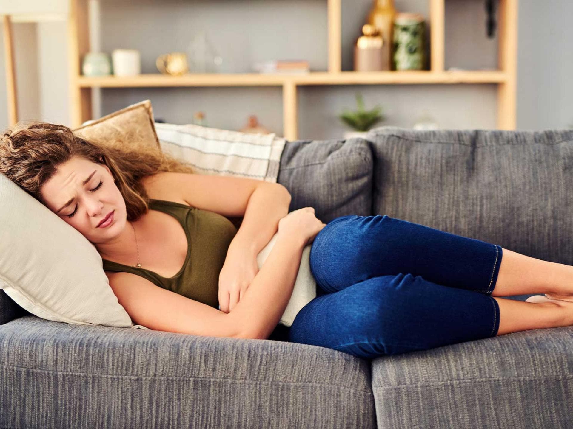 Frau liegt mit Bauchschmerzen auf dem Sofa.