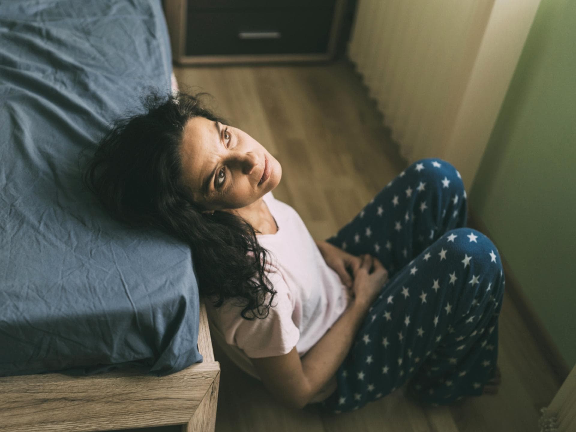 Die Perimenopause kann man aufgrund ihrer Symptome schon mal mit einer Frühschwangerschaft verwechseln. Frau sitzt vorm Bett und starrt an die Decke.