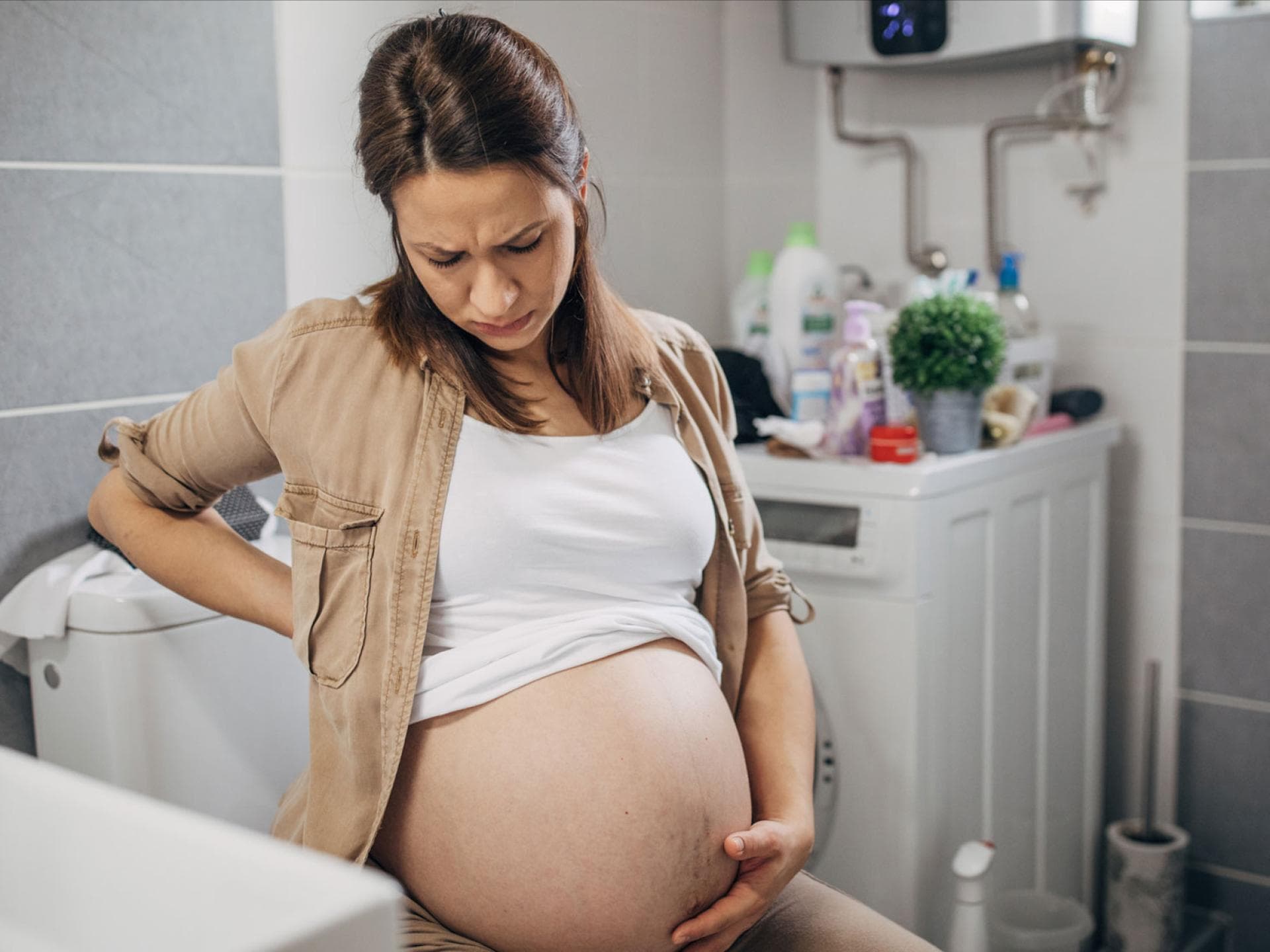 Starker Harndrang ist das häufigste Symptom einer Blasenentzündung – das gilt auch in der Schwangerschaft. Außerdem schmerzt und brennt es beim Wasserlassen. Schwangere Frau mit Schmerzen auf der Toilette.