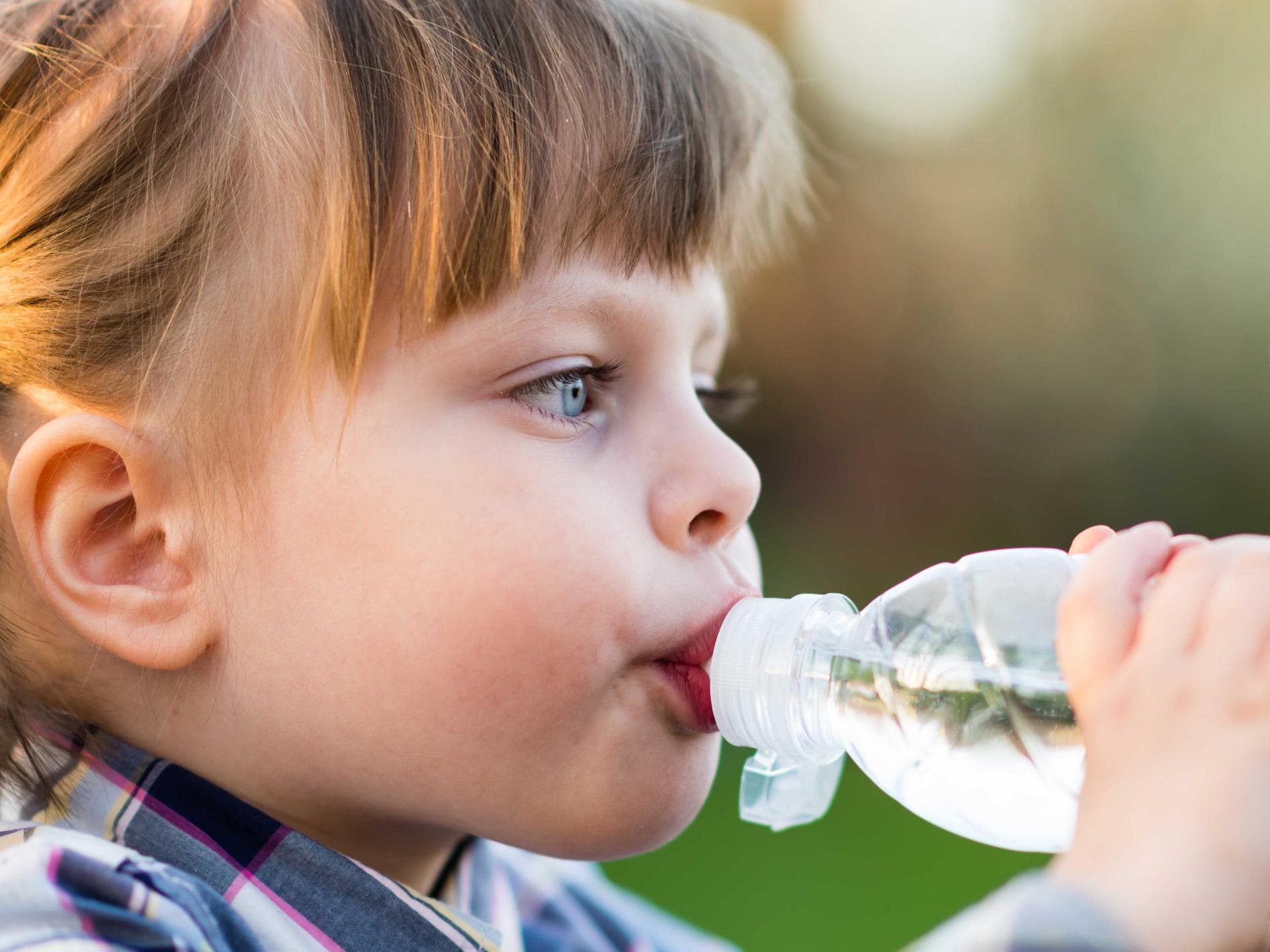 Gerade im Sommer ist es wichtig, dass Kinder ausreichend trinken. Mädchen trinkt aus einer Wasserflasche.