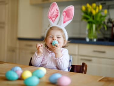 Ein kleines Mädchen lächelt und hat ein gefärbtes Osterei in der Hand.