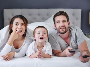 2-Jähriger guckt mit seinen Eltern einen Kinderfilm vom Bett aus