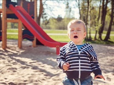 Kleiner Junge sitzt weinend vor einer Rutsche im Sand