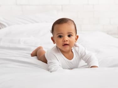 Ein Baby krabbelt auf dem Bett.