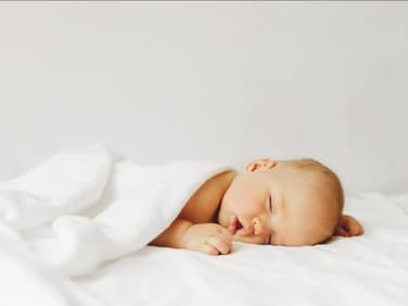 Baby schläft zugedeckt auf dem Bett.