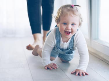 Kleines Mädchen krabbelt grinsend über den Fußboden.