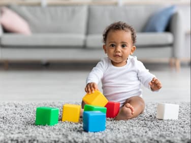 Ein kleiner Junge sitzt auf dem Boden und spielt mit Bauklötzen.