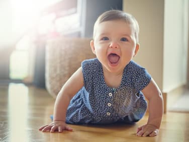 Baby-Mädchen robbt auf dem Boden und lacht mit offenen Mund.