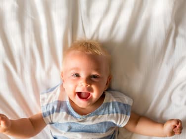 Baby-Junge liegt auf dem Bett und lacht.