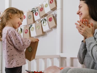 Kleines Mädchen öffnet ihren Montessori-Adventskalender. Und Mama freut sich mit!