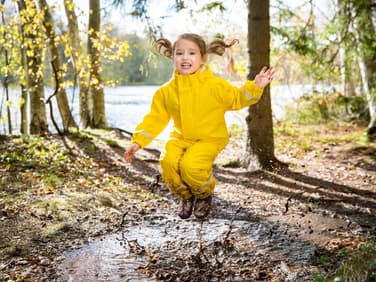 Kind spielt draußen und springt in Pfütze