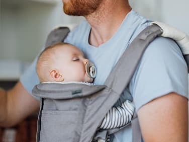 Ein Baby schläft bei Papa in der Trage mit Schnuller