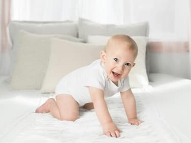 Ein kleiner Junge kniet auf dem Bett.