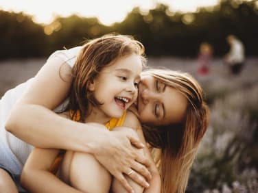 Mutter umarmt ihre Tochter auf der Wiese.