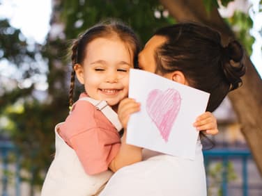 Ein Mädchen mit einer Postkarte in der Hand auf dem Arm ihres Vaters. 