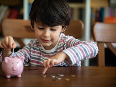 Junge steckt Geld in sein Sparschwein.