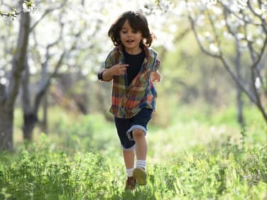 Junge rennt unter Obstbäumen über eine grüne Frühlingswiese.