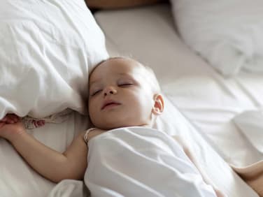 Baby schläft in einem Bett mit großen Kissen.