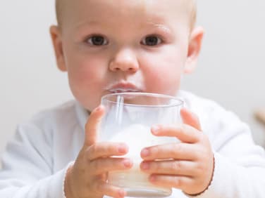 Kleinkind trinkt Milch aus dem Glas.