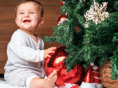 Genau so soll es an Weihnachten sein: Das Baby lacht vergnügt unterm geschmückten Baum.