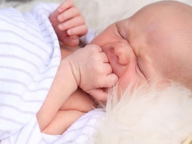 Baby liegt bei sommrlichen Temperaturen auf einem Lammfell