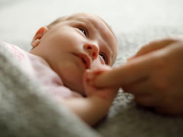 Müdes Baby hält Finger eines Elternteils.