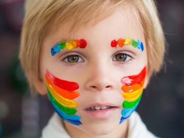 Junge mit geschminktem Regenbogen auf Wangen und Augenbrauen