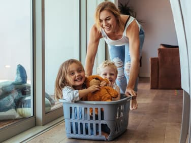 Mutter schiebt ihre Kinder im Wäschekorb.
