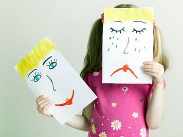 Gefühle zeigen: Kind hält gemaltes, trauriges Gesicht vor ihr eigenes.